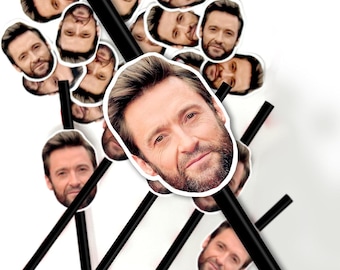 May include: A collection of black straws topped with white stickers featuring a celebrity's face. The stickers are in various orientations, creating a playful and unique design. The background is plain white.