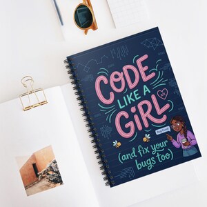 May include: A spiral-bound notebook with a navy blue cover featuring the text "CODE LIKE A GIRL (and fix your bugs too)" in pink and teal. The design includes circuit board graphics and illustrations of bees and a girl with glasses.
