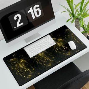 May include: A black and gold computer mouse pad with a circuit board design. A white keyboard and mouse sit on the pad. A computer monitor displays the time as 2:16 PM. A plant is in the background.
