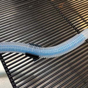 May include: A clear, flexible tube with a blue interior, held in place by a black clip. The tube is on a black, slatted surface. The end of the tube has a clear, plastic connector.