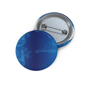 May include: Two round blue buttons with a metal pin backing. The front of the buttons have a gradient blue background with a light blue technical drawing design. One button is face up, and the other is face down.