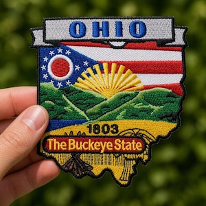 May include: Embroidered patch featuring the Ohio state flag design. The patch includes the word "OHIO" in blue, a red and white striped section, and a blue field with white stars. The patch also features the text "1803" and "The Buckeye State".