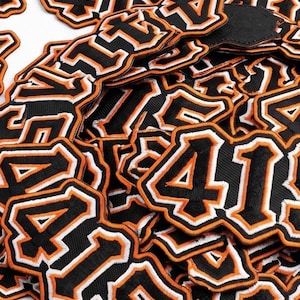 415 embroidered patch featuring bold varsity-style numbers with black, white, and orange outline design. High-quality stitched number patch inspired by streetwear and urban fashion, perfect for jackets, hoodies, hats, and backpacks.
