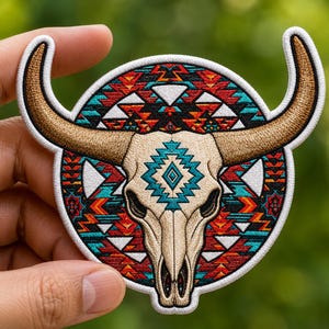 May include: Embroidered patch featuring a bull skull with large brown horns. The skull is cream-colored, with a turquoise and cream geometric design in the center. The background is a circular pattern of red, turquoise, and orange geometric shapes.