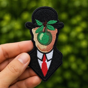 May include: Embroidered patch with a surreal design inspired by René Magritte's "The Son of Man." The patch shows a man in a bowler hat with a green apple covering his face. The man is wearing a black suit with a red tie.