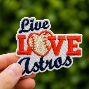 May include: Embroidered patch with the words "Live Love Astros" in navy blue and orange. The word "Love" features a baseball-shaped heart. The patch is white with an orange border.