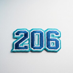 May include: Embroidered patch featuring the number "206" in a bold, collegiate style. The numbers are dark blue with a light blue outline and white stitching, creating a layered effect. The patch is likely for a jacket or bag.