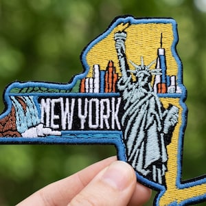 May include: Embroidered patch in the shape of New York State, featuring the Statue of Liberty, city skyline, and the text "NEW YORK." The patch has a yellow background, blue border, and detailed stitching.