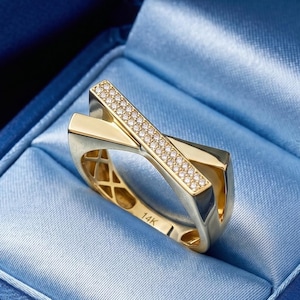 May include: A gold ring with a crisscross design, set with small diamonds. The ring is displayed in a blue velvet jewelry box. The ring is marked with "14K".
