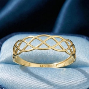 Op de afbeelding: Een goudkleurige ring met een open ontwerp van verweven ruitvormen. De ring ligt op een lichtblauwe ondergrond in een donkerblauwe sieradendoos. De ring is gemarkeerd met "14K".