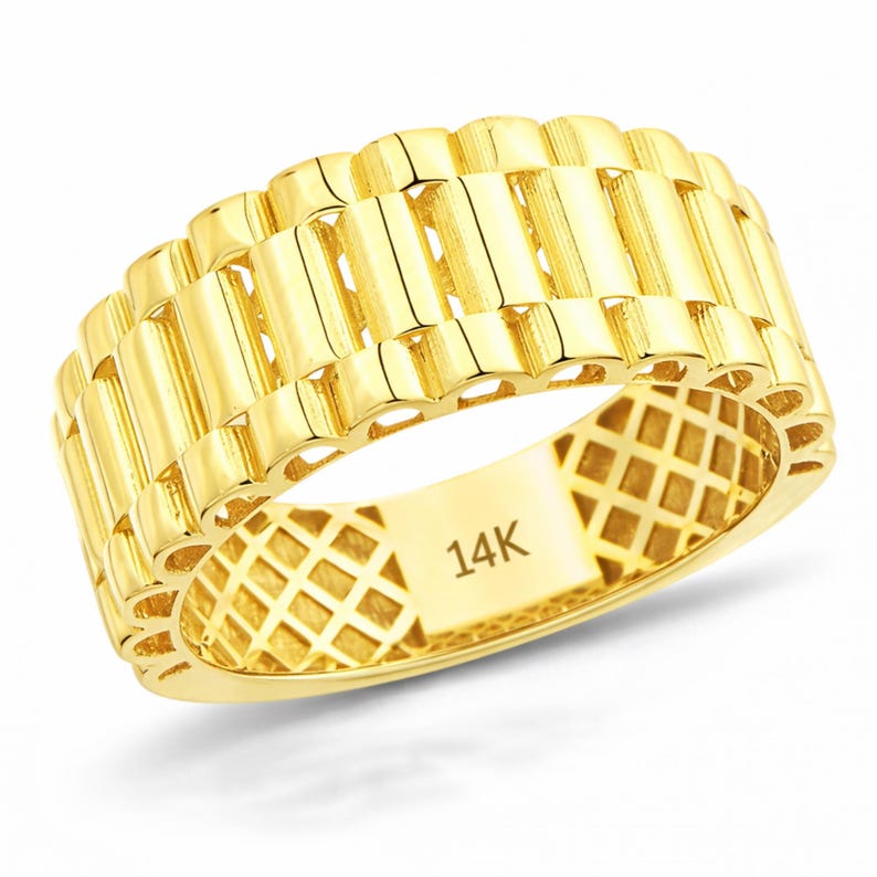 May include: A gold-colored ring with a textured, watch-band style design. The ring is made of 14K gold and features a repeating pattern of vertical bars. The inside of the ring has a diamond-shaped pattern and the text "14K".