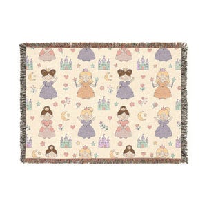 May include: A cream-colored throw blanket featuring a repeating pattern of cartoon princesses in various dresses, castles, moons, stars, and flowers. The blanket has a fringed edge and is suitable for a child's room or nursery.