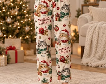Pode incluir: Calças de pijama em tom creme com um padrão natalício repetitivo de gatos com gorros de Pai Natal e cachecóis, ornamentos vermelhos e pegadas. O texto AMANDA'S CATMAS está impresso nas pernas, juntamente com os nomes LUNA e MILO.