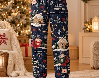 Pode incluir: Calças de pijama azul-marinho com uma estampa de Natal com casas nevadas, canecas de chocolate quente, pinheiros, corações vermelhos e flocos de neve. O texto diz ALEX + MORGAN CLOSER EVERY CHRISTMAS e DECEMBER 24, 2026.