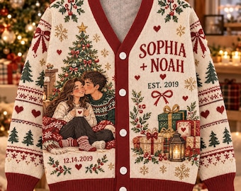 Pode incluir: Um cardigã de malha cor de creme com decote em V e punhos vermelho-escuros. A frente apresenta um casal, uma árvore de Natal, presentes e o texto 'SOPHIA + NOAH', 'EST. 2019' e '12.14.2019'. Tem cinco botões brancos e um padrão festivo.