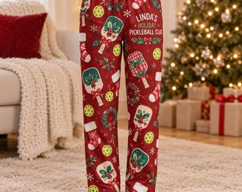 Pode incluir: Calças de pijama vermelhas com um padrão repetitivo de raquetes de pickleball, bolas amarelas, meias de Natal e guirlandas. O texto "LINDA'S HOLIDAY PICKLEBALL CLUB" está impresso na perna direita em letras brancas.