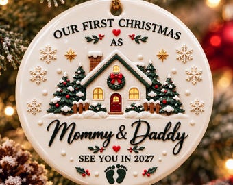 Pode incluir: Um enfeite de Natal redondo em cerâmica branca com ilustração de casa, pinheiros verdes e flocos de neve. Texto: OUR FIRST CHRISTMAS AS Mommy & Daddy SEE YOU IN 2027. Inclui corações vermelhos, uma guirlanda e pegadas de bebê.