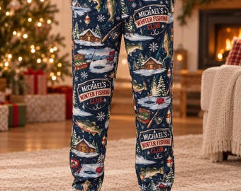 Pode incluir: Calças de pijama azul-marinho com um padrão repetitivo de peixes, cabanas com neve, equipamento de pesca e flocos de neve. O tecido inclui etiquetas com o texto "Michael's Winter Fishing Club" num emblema retangular branco e vermelho.