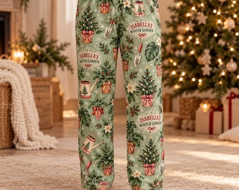 Pode incluir: Calças de pijama verde-claras com um padrão repetitivo de árvores de Natal em vasos, regadores, pás de jardim e poinsétias. A estampa inclui o texto Isabella's Winter Garden em uma fonte decorativa.