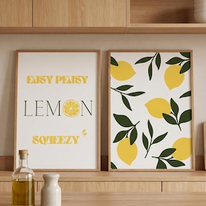 Könnte beinhalten: Zwei gerahmte Kunstdrucke mit Zitronenmotiv. Ein Druck zeigt den Text "Easy Peasy Lemon Squeezy" und eine Zitronenscheibe. Der andere Druck zeigt ein Muster aus gelben Zitronen und grünen Blättern auf weißem Hintergrund.