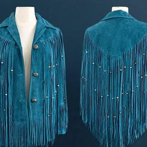 May include: Teal suede jacket with long fringe and decorative beading. The jacket features a collared neckline, three buttons, and fringe detailing along the front, back, and sleeves. A stylish, bohemian-inspired piece.