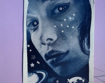 May include: A cyanotype print on paper featuring a monochromatic blue portrait of a person with dark hair. The image is overlaid with white graphic elements including various sizes of stars, a crescent moon, a planet with rings, and a globe.