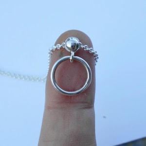 Könnte beinhalten: Eine silberne Halskette mit einem kleinen, runden Anhänger und einem daran befestigten Ring.