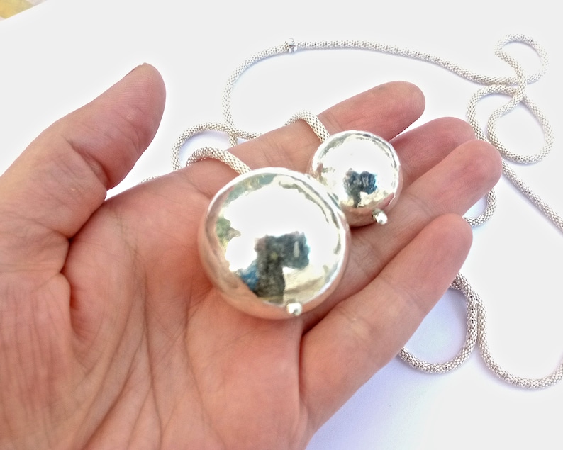 May include: A silver necklace with two round, smooth, silver pendants. The necklace is made of a fine chain.