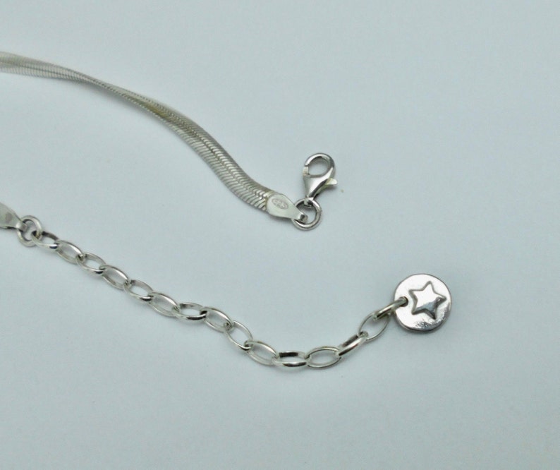 K&ouml;nnte beinhalten: Eine silberne Kettenkette mit einem kleinen Sternanh&auml;nger. Die Kette besteht aus zwei verschiedenen Stilen, einer Schlangen- und einer Gliederkette.