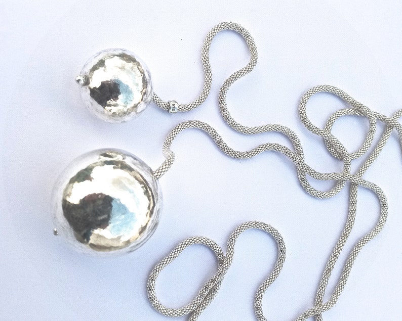May include: A silver chain necklace with two large, round, hammered silver pendants.