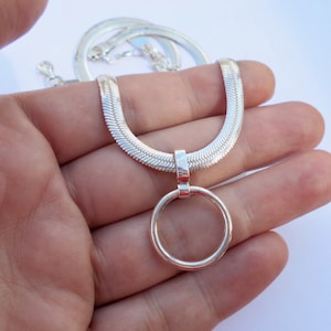 May include: A silver-toned herringbone chain necklace featuring a smooth, circular pendant attached to a polished bail. The flat, woven links of the chain create a sleek, reflective surface that leads to the simple, open ring charm at the center.