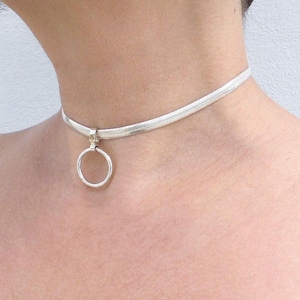 May include: A silver-toned choker necklace featuring a flat, flexible herringbone chain design. The necklace includes a central circular ring pendant attached to the chain by a small, fixed metal bail, resting securely against the base of the neck.