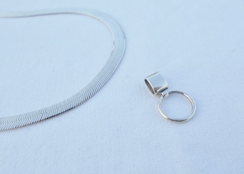 May include: A silver chain necklace with a silver pendant featuring a round ring. The chain is a herringbone style.