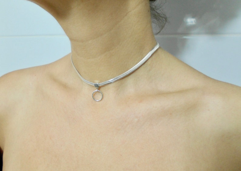 K&ouml;nnte beinhalten: Eine silberne Choker-Kette mit einem kleinen, runden Anh&auml;nger.