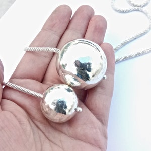 May include: A silver necklace with two hammered silver spheres as pendants. The necklace is made of a delicate chain.