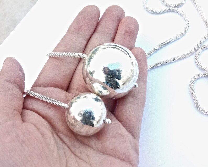 May include: A silver necklace with two hammered silver spheres as pendants. The necklace is made of a delicate chain.