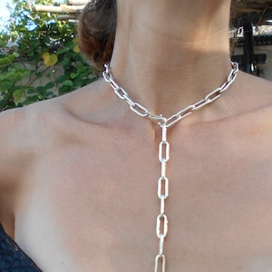 Puede incluir: Un collar de cadena de plata con un largo colgante. La cadena está hecha de eslabones ovalados.