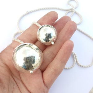 May include: A silver necklace with two large, round, hammered silver pendants. The necklace is made of a delicate chain.