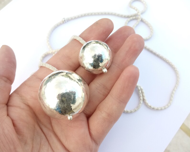 May include: A silver necklace with two large, round, hammered silver pendants. The necklace is made of a delicate chain.