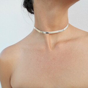 Pu&ograve; includere: Un girocollo in argento con una fascia piatta e larga.