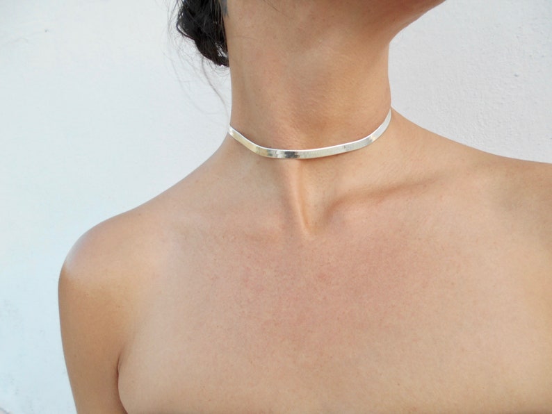 Pu&ograve; includere: Un girocollo in argento con una fascia piatta e larga.