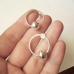 May include: A pair of silver hoop earrings with a small silver ball hanging from each hoop.
