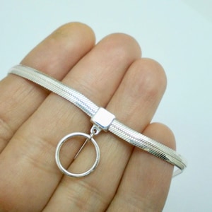 Puede incluir: Un collar gargantilla de plata con un diseño de cadena de serpiente y un colgante circular.