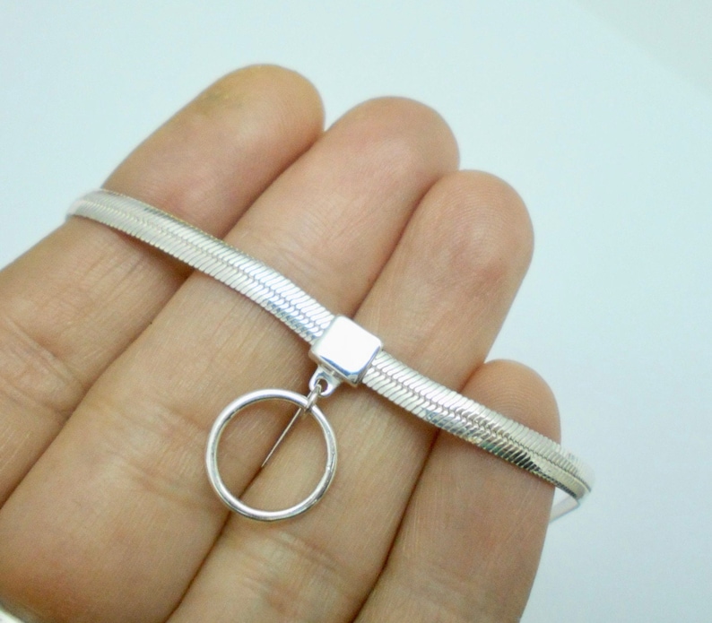 K&ouml;nnte beinhalten: Eine silberne Choker-Kette mit Schlangenketten-Design und einem baumelnden Kreis-Anh&auml;nger.