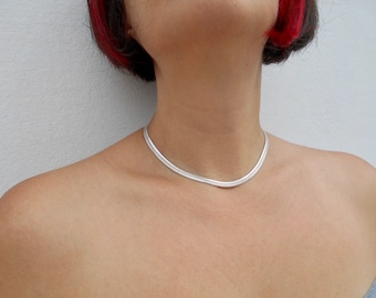 May include: A silver chain necklace with a simple, sleek design. The necklace is worn by a person with red hair.