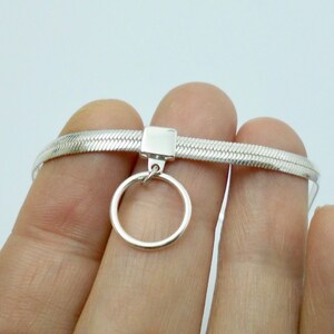 K&ouml;nnte beinhalten: Eine silberne Choker-Kette mit einem Schlangenketten-Design und einem kleinen runden Anh&auml;nger.