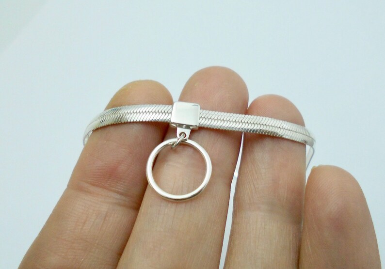 K&ouml;nnte beinhalten: Eine silberne Choker-Kette mit einem Schlangenketten-Design und einem kleinen runden Anh&auml;nger.
