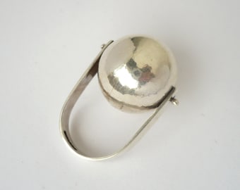 Puede incluir: Un anillo de plata con una bola grande, redonda y lisa que gira sobre una banda.