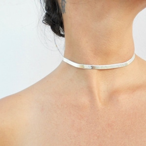 May include: A silver choker necklace with a flat, thin design. The necklace is simple and elegant, and would make a great addition to any jewellery collection.