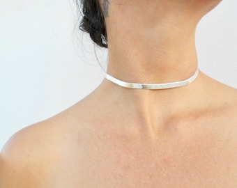 May include: A silver choker necklace with a flat, thin design. The necklace is simple and elegant, and would make a great addition to any jewelry collection.